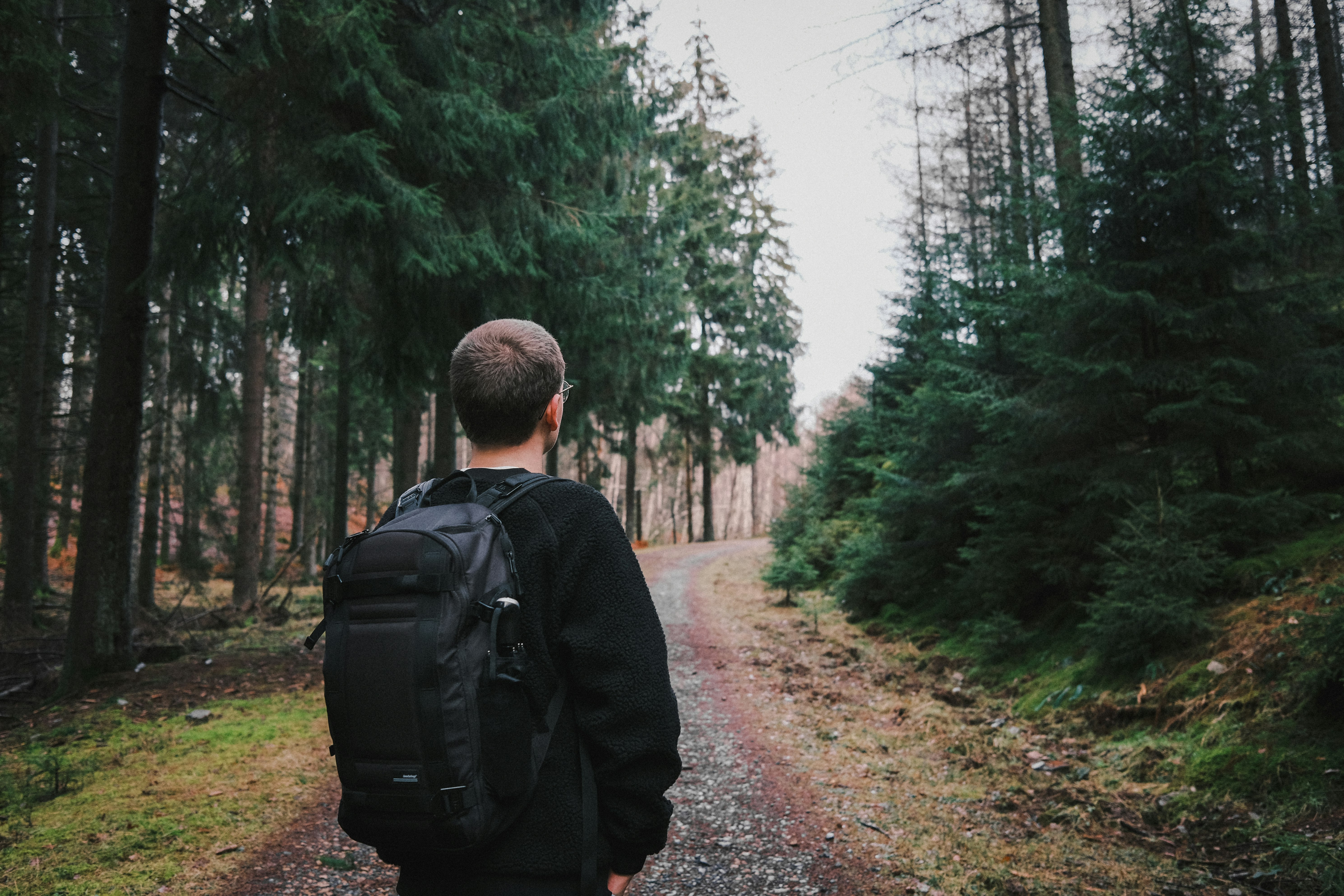 man in black jacket walking on pathway between trees during daytime